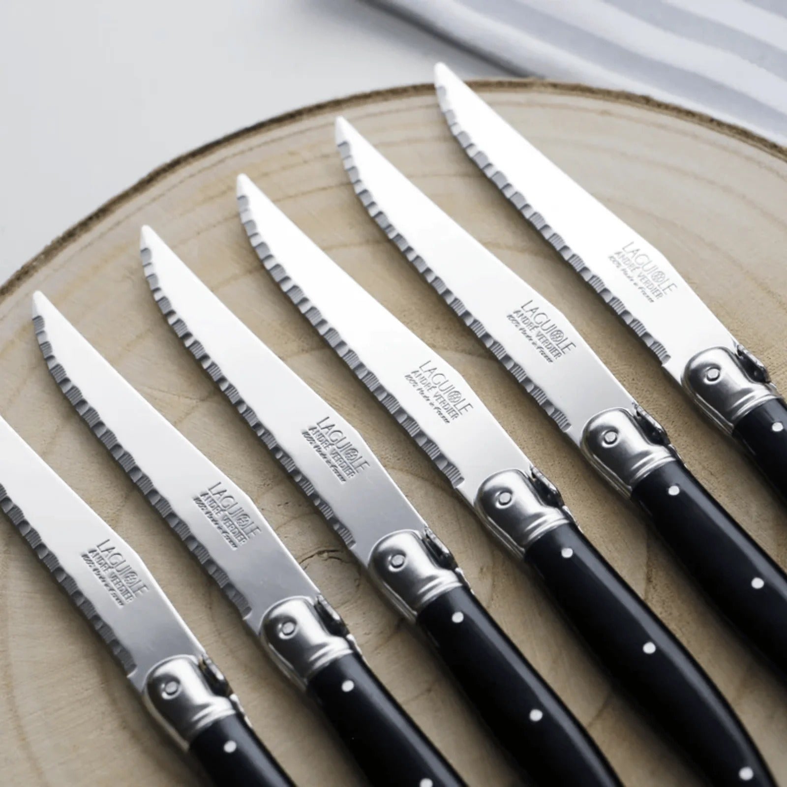 Andre Verdier Laguiole steak knives with black handles fanned out on a wooden board