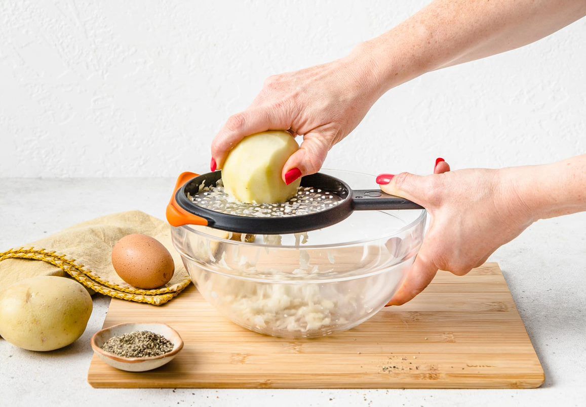 Dreamfarm Ograte coarse grater with orange handle, grating potato over a glass bowl