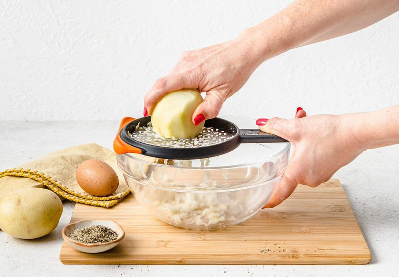 Dreamfarm Ograte coarse grater with orange handle, grating potato over a glass bowl