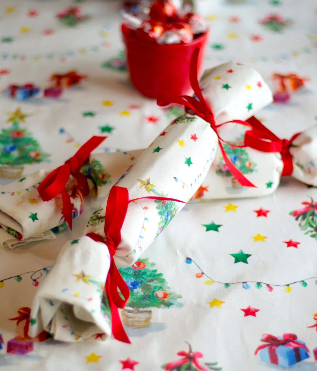 Three rolled Christmas crackers with red ribbon bows, wrapped in white paper printed with colorful stars and Christmas trees