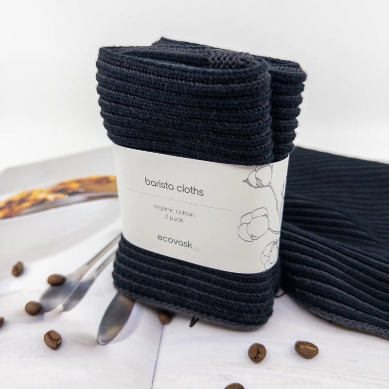 Pack of black barista cloths with a label on a white surface with coffee beans and a spoon.