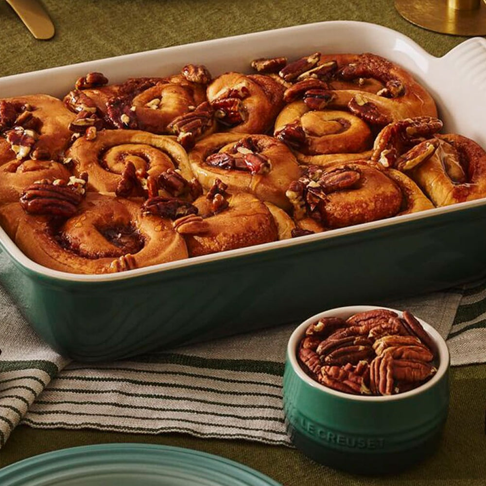 Pecan cinnamon scrolls baked in a green Le Creuset stoneware dish, with a small dish of pecans alongside