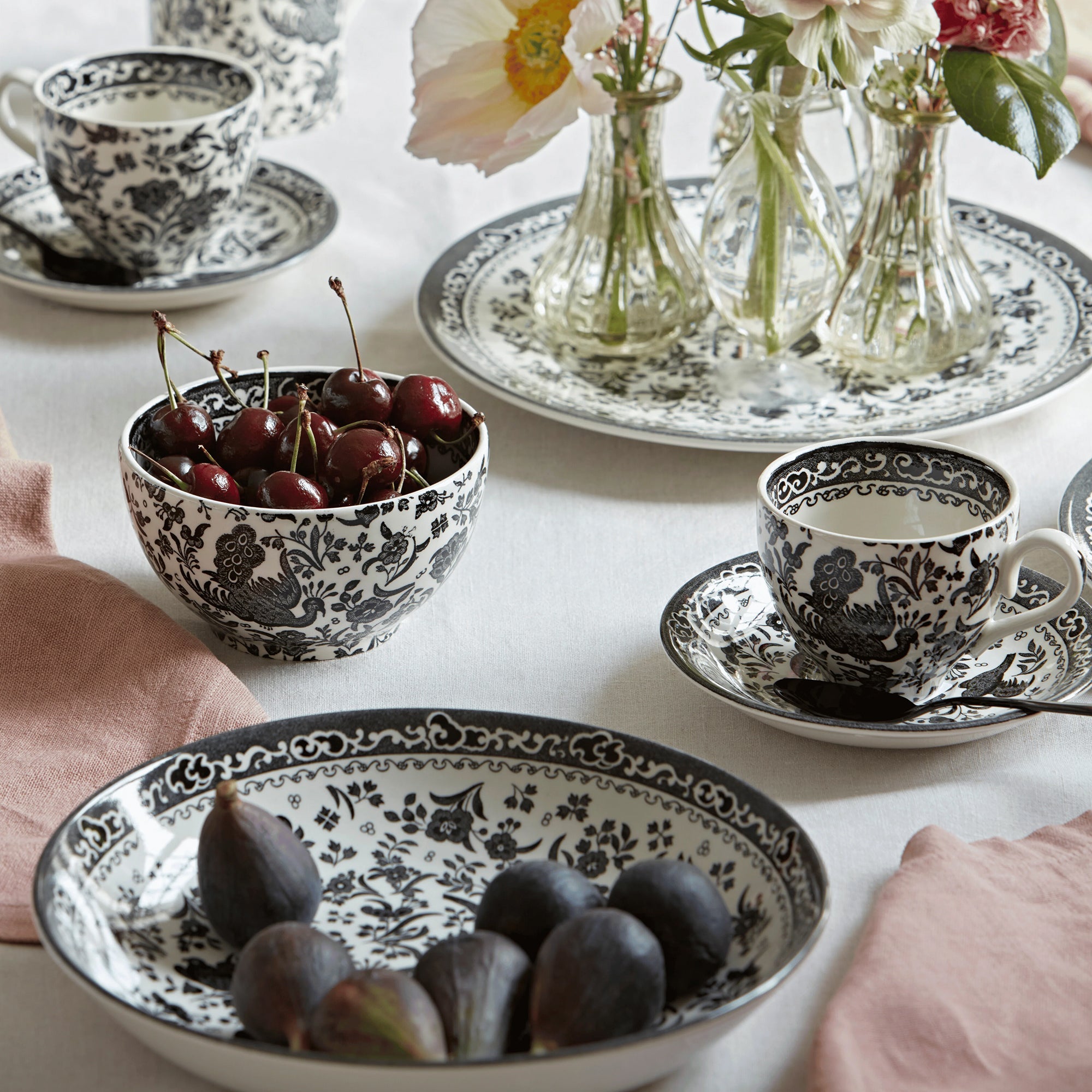 Black and white floral patterned ceramic plates and bowl styled with glazed cinnamon rolls, silver forks, and a cup of tea on a rustic wooden surface