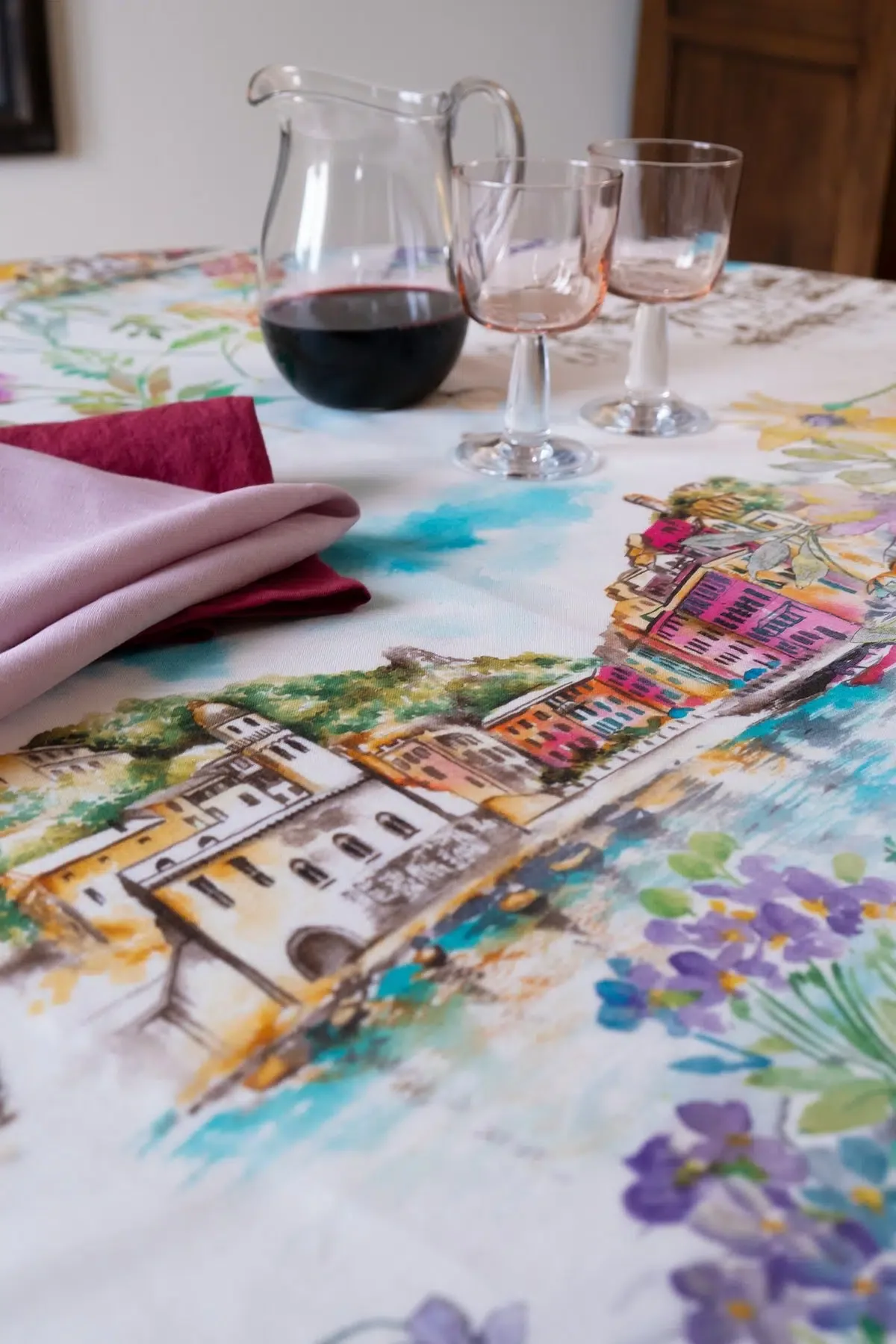 A close-up of a printed tablecloth with a colorful watercolor-style scene of buildings and flowers.