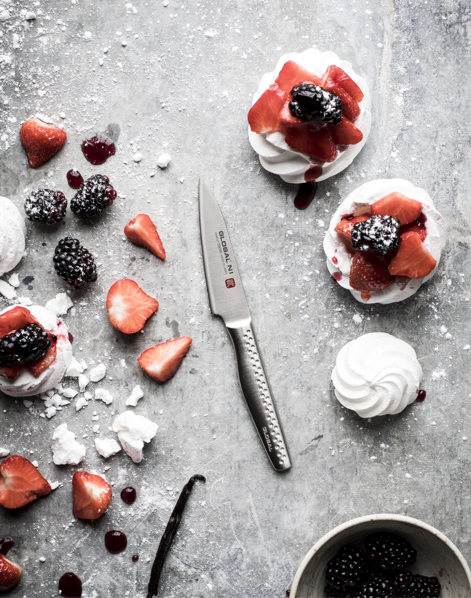 Global NI utility knife slicing strawberries beside mini pavlovas with blackberries and cream