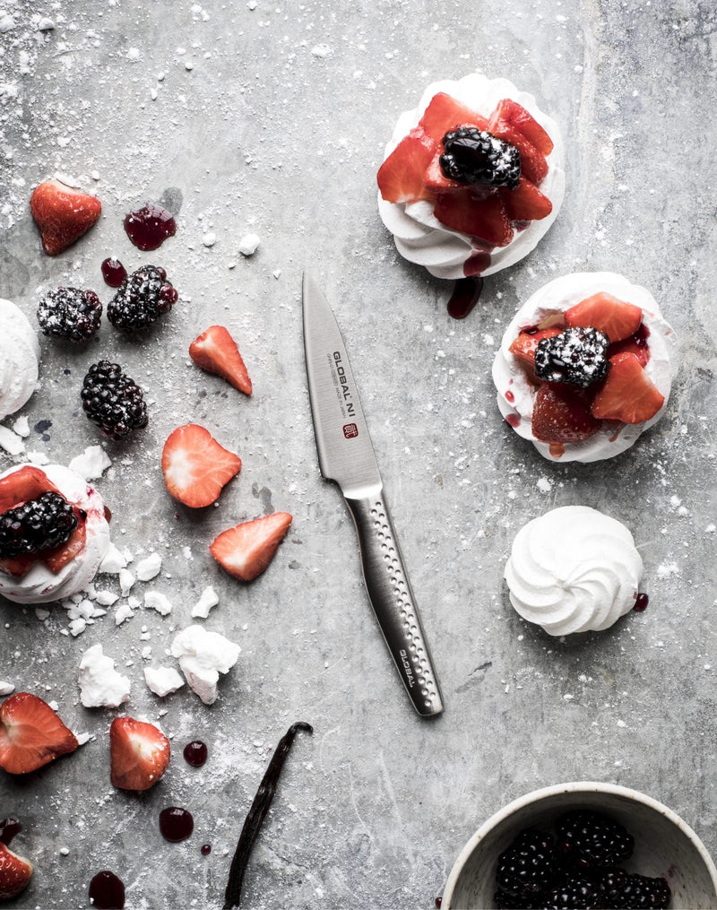 Global NI utility knife slicing strawberries beside mini pavlovas with blackberries and cream