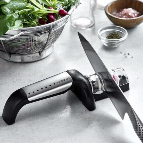 Global G2 20cm cook's knife and sharpener set, with a knife being sharpened on a black sharpener