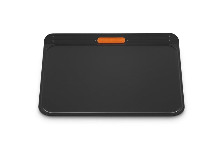 Le Creuset insulated cookie sheet in black with an orange corner grip