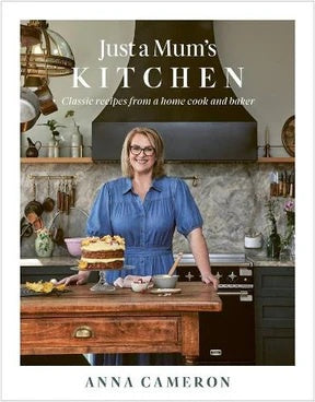 Just a Mum's Kitchen cookbook by Anna Cameron, with the author standing in a kitchen holding a layer cake