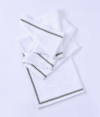 MM Linen embroidered table cloth in white with a green zigzag edge, shown folded with matching napkins