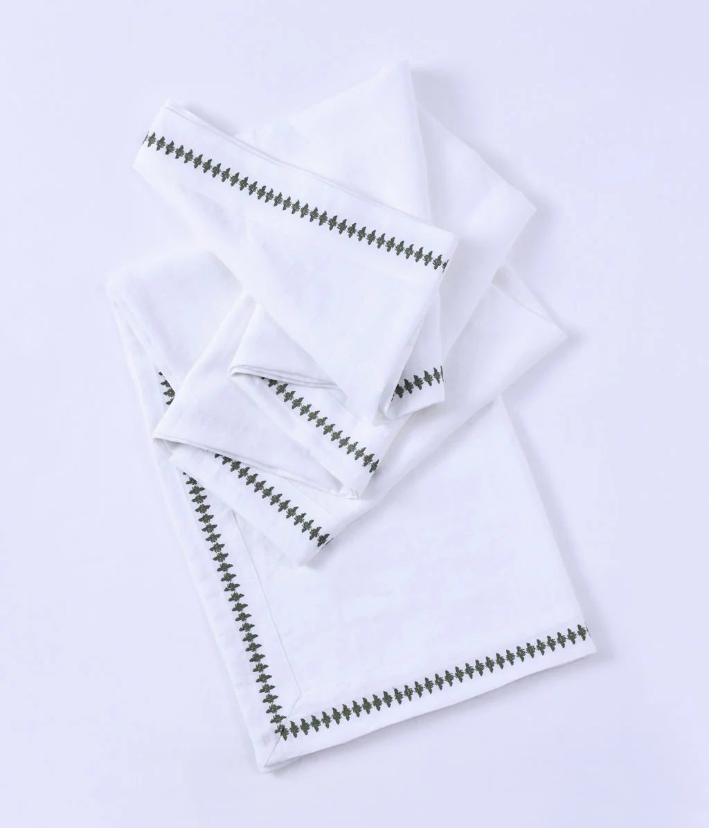 MM Linen embroidered table cloth in white with a green zigzag edge, shown folded with matching napkins