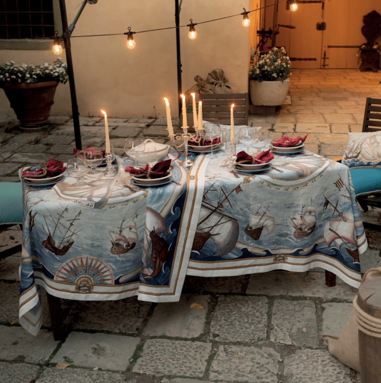 Tessitura Toscana Telerie Bounty linen tablecloth with a ship print, styled on an outdoor candlelit table