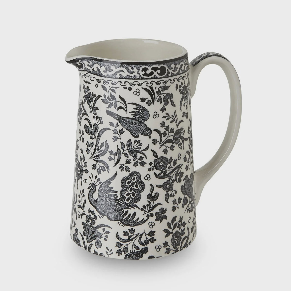 A ceramic pitcher with a black and gray floral and bird pattern on a white background