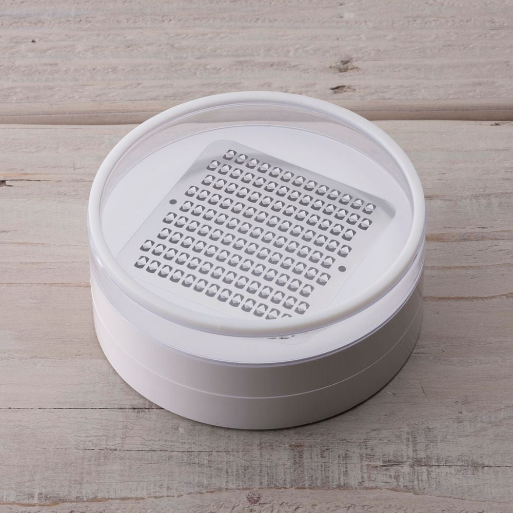 Kai Select 100 micro grater, a round white grater with a clear lid and a stainless steel etched plate