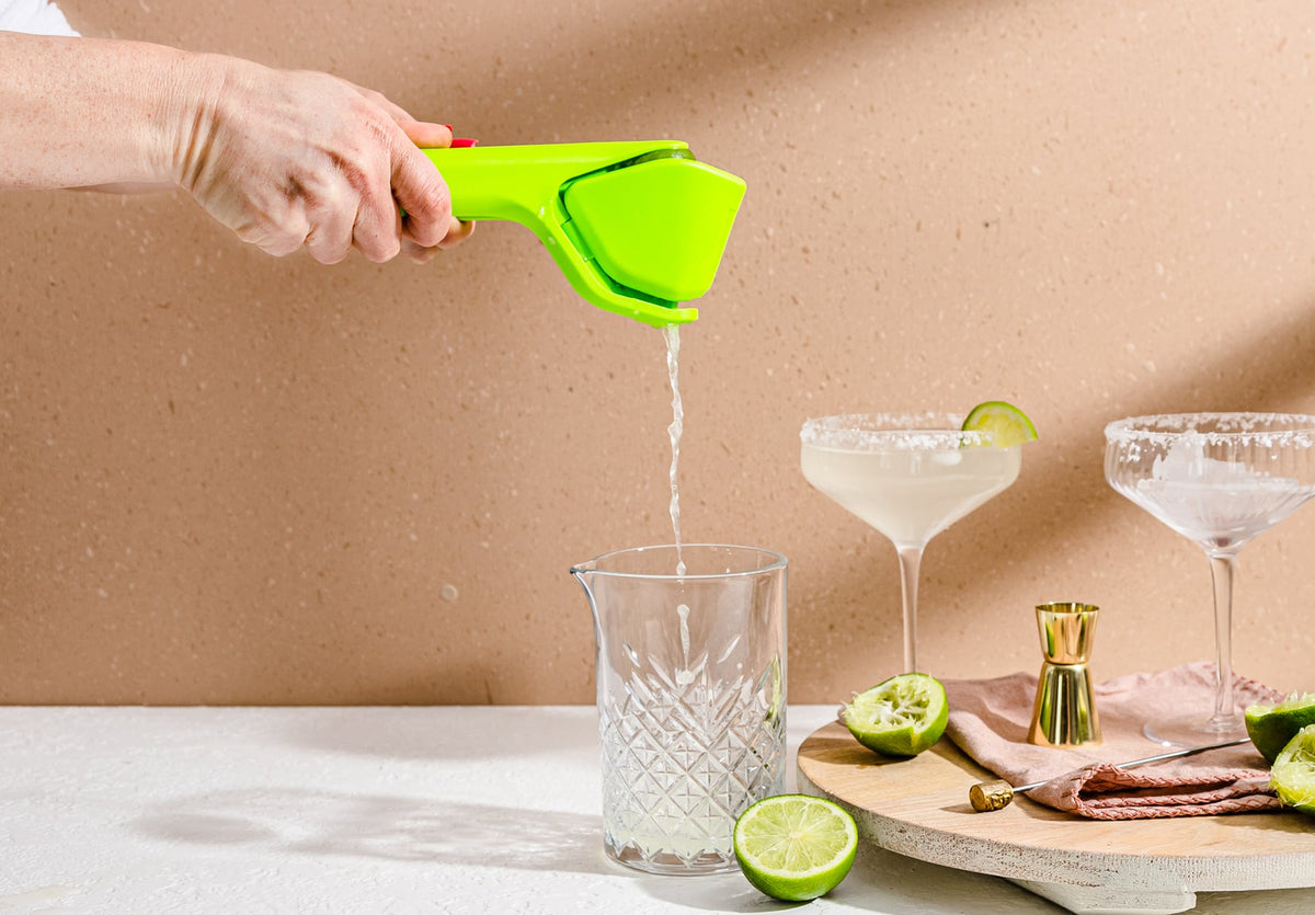 Dreamfarm Fluicer lime squeezer in bright green, shown pouring juice into a glass at a cocktail table