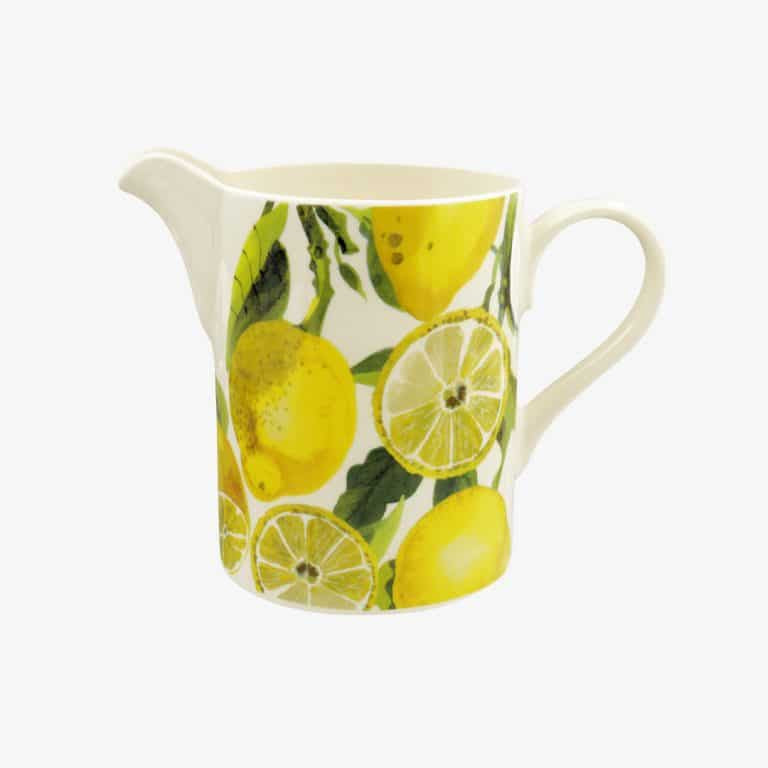 A white ceramic pitcher decorated with a vibrant yellow lemon and lime slice pattern with green leaves, shown against a plain light gray background.