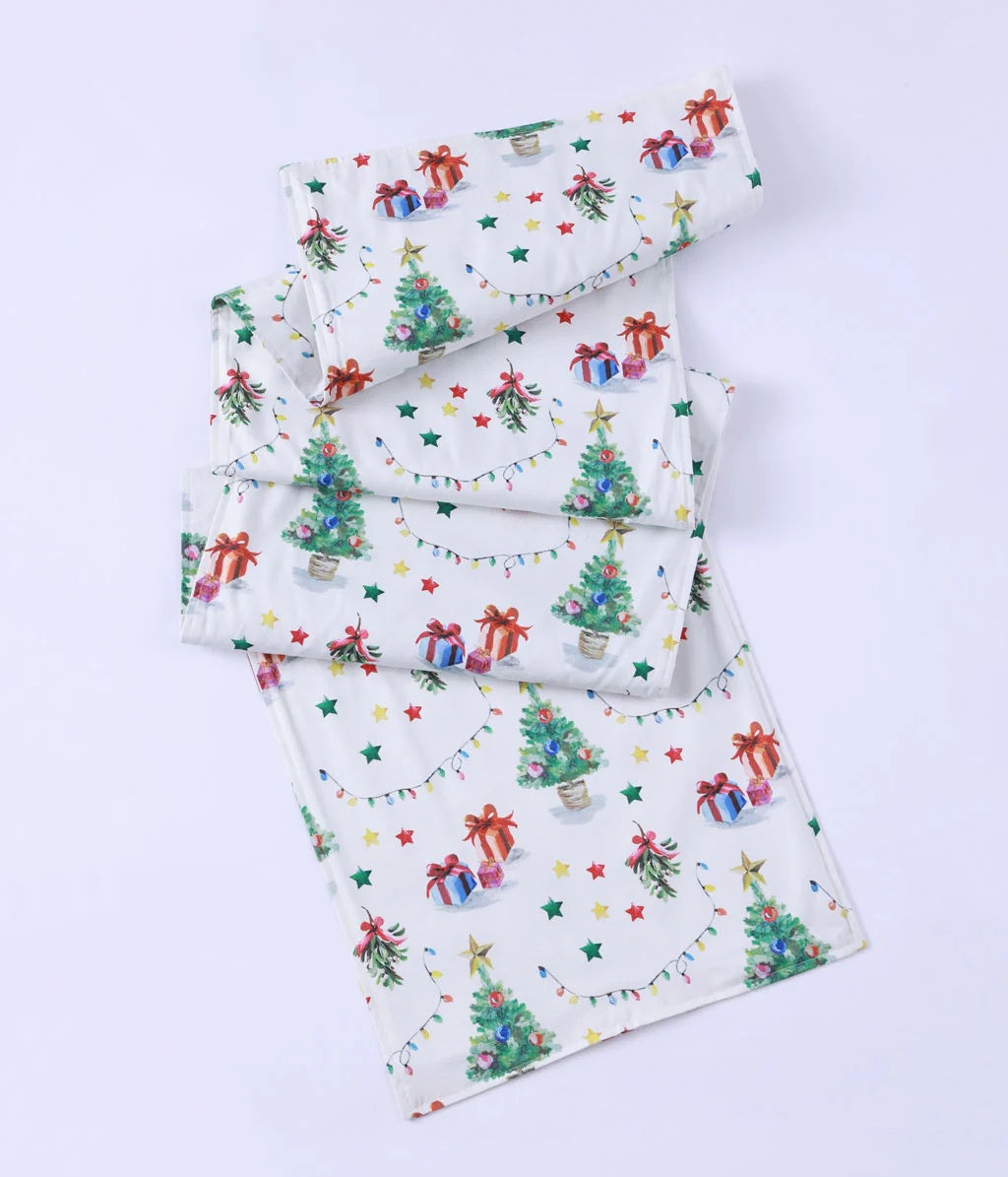 MM Linen Feliz Navidad table runner in white with Christmas trees, presents and stars