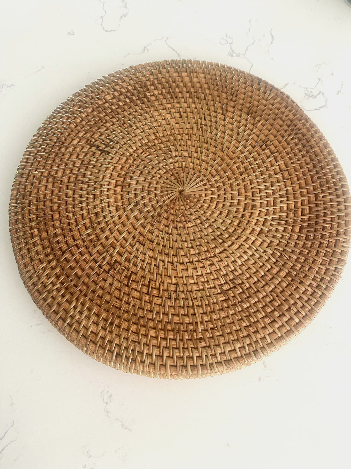 Barville natural rattan round placemat in brown, shown on a white marble surface