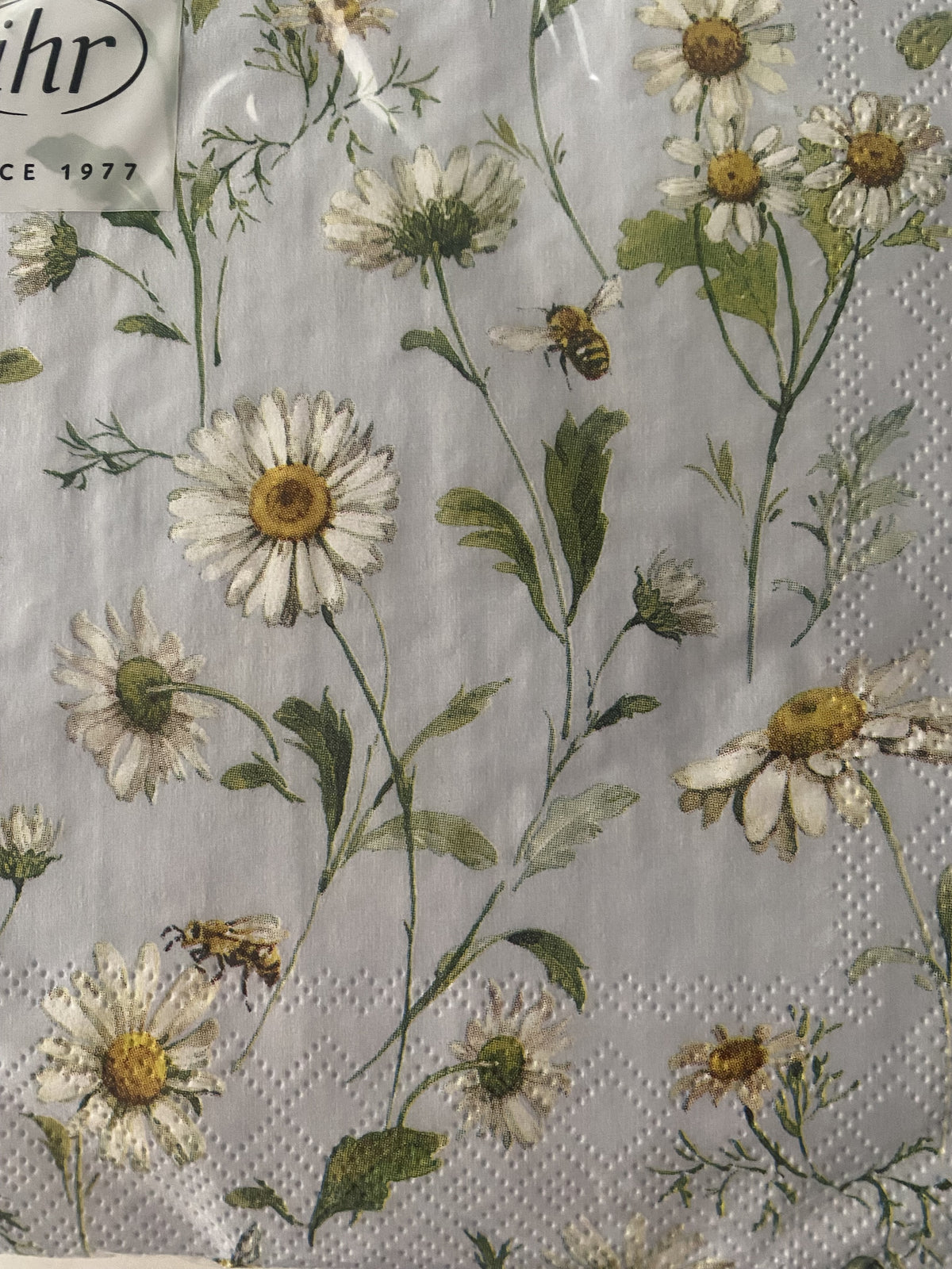 IHR cocktail napkin with daisies and a bee on a light blue-grey background