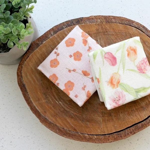 Nawrap face cloths in orange blossom and tulip prints, shown folded on a wooden slice