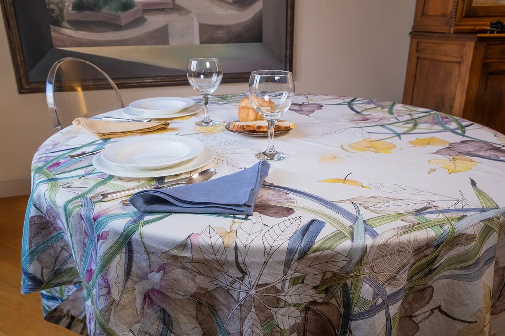 Telene Orchidea tablecloth with an orchid floral print, styled on a round table with place settings and wine glasses