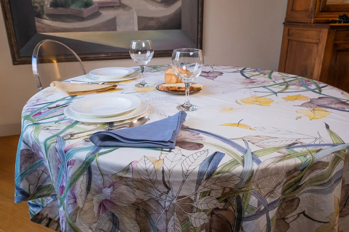 Telene Orchidea tablecloth with an orchid floral print, styled on a round table with place settings and wine glasses