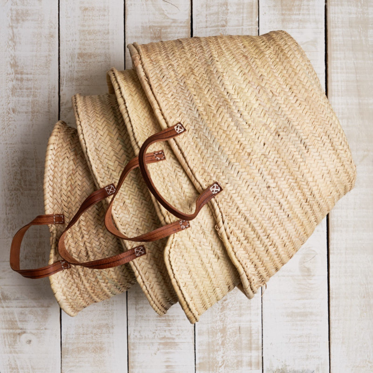 French market baskets with flat leather handles, shown nested in natural woven straw