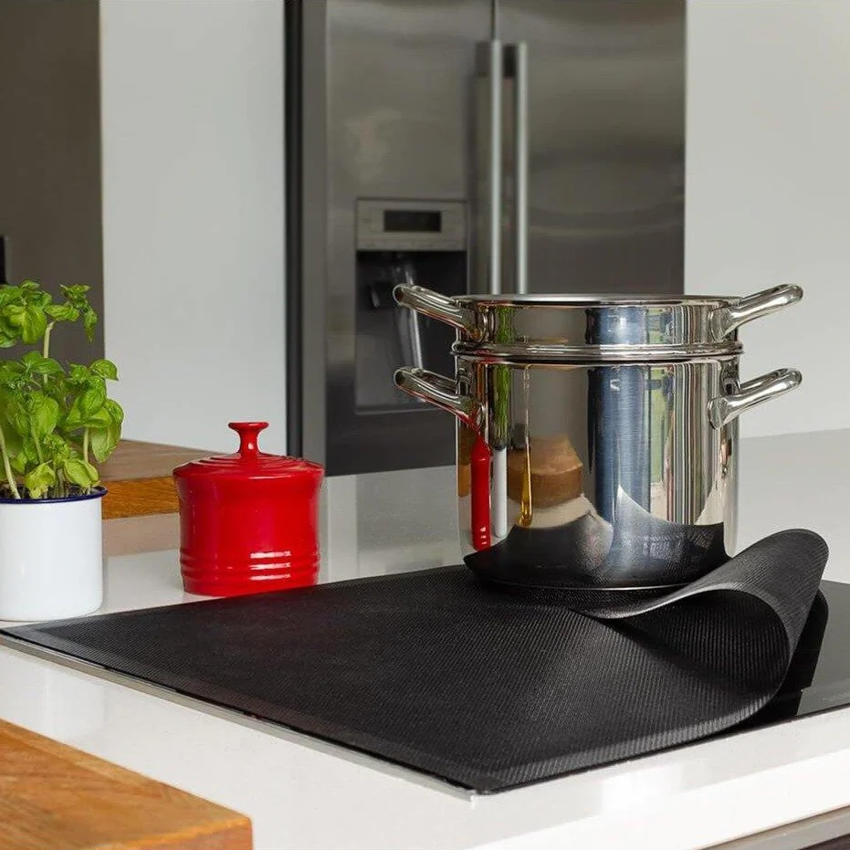 Bake-O-Glide induction hob protector, a black mat on a cooktop under a stack of steel pots