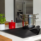 Bake-O-Glide induction hob protector, a black mat on a cooktop under a stack of steel pots