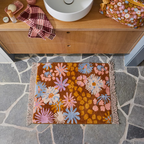 Sage x Clare Hayfolk bath mat with a tufted daisy pattern in orange, pink and blue, on a stone bathroom floor