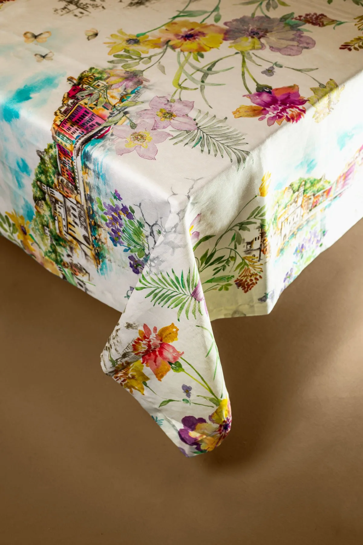 Telene Borghi Village linen tablecloth with a print of colourful flowers and a village scene, on a table