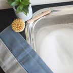 Nawrap ribbed dishcloth in blue and grey draped over a sink beside a wooden dish brush